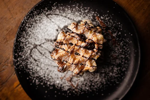 Delicious waffle drizzled with chocolate sauce and dusted with powdered sugar on a black plate.