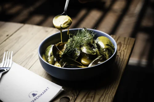 Bowl of mussels with creamy sauce, garnished with dill, served on a wooden table.