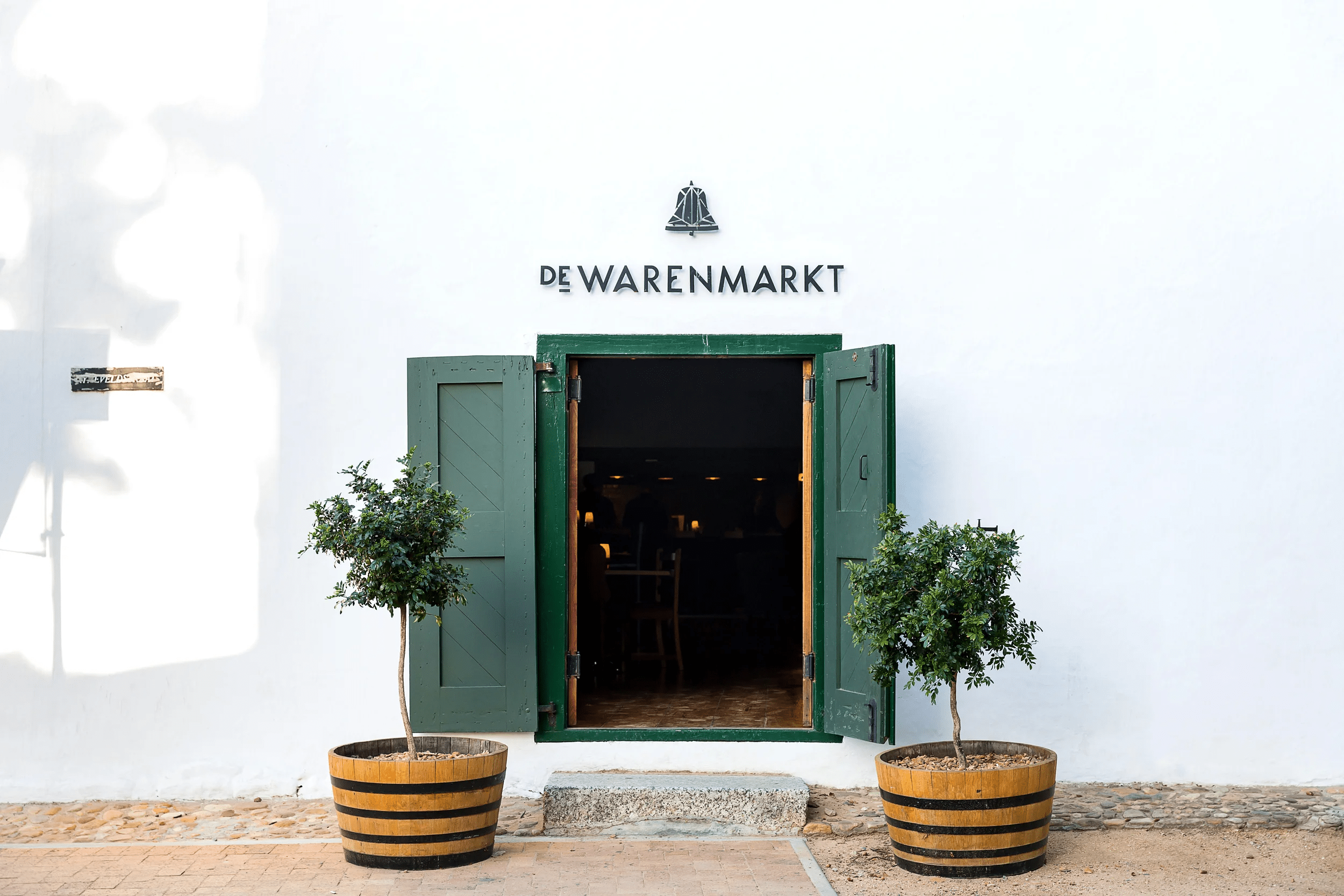 De Warenmarkt building entrance with open green doors and potted trees.