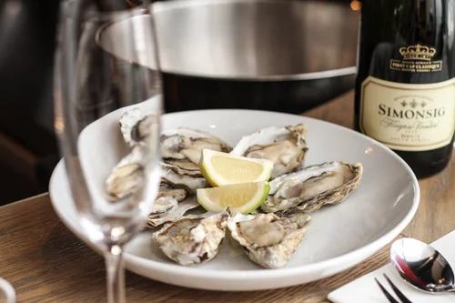 Fresh oysters on a white plate with lemon wedges and a bottle of Simonsig wine