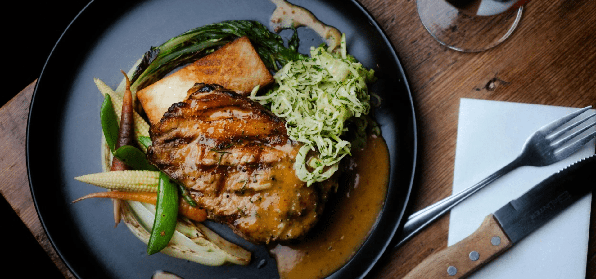 Grilled pork chop with roasted vegetables and sauce on a black plate
