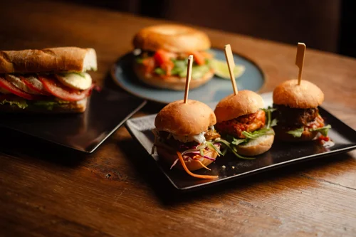 Assortment of mini burgers and a sandwich on a wooden table