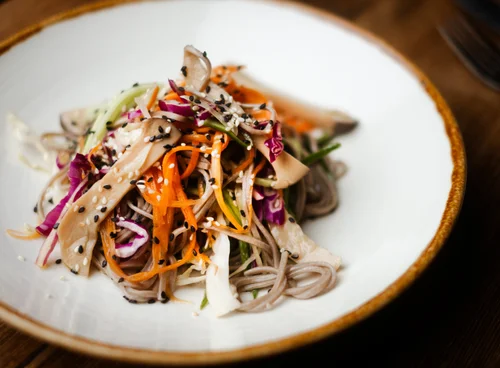 Soba noodle salad with shredded vegetables and sesame seeds on a white plate