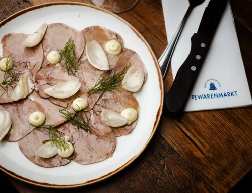 Thinly sliced beef tongue with white sauce and dill on a white plate