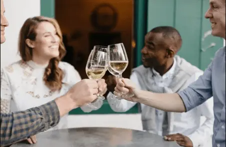 Four friends toasting with white wine glasses at an outdoor table.
